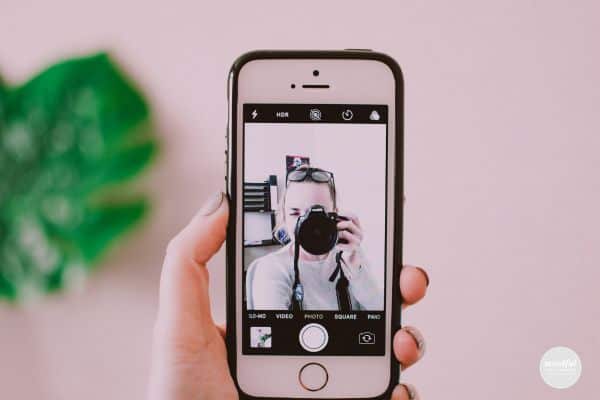 woman taking a picture of herself on her iphone, unlocking her hidden potential as a content creator.