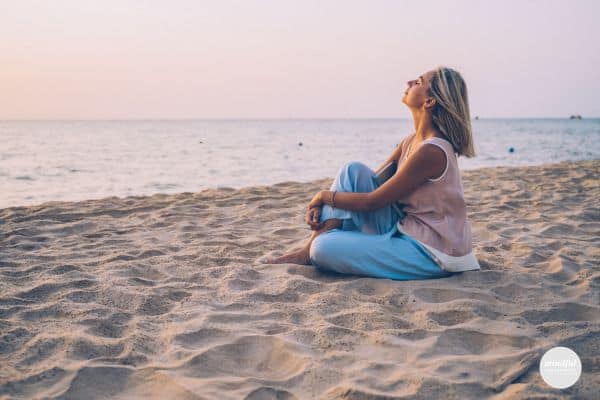 middle age woman sitting on the beach practicing grounding exercises for peace and calm.